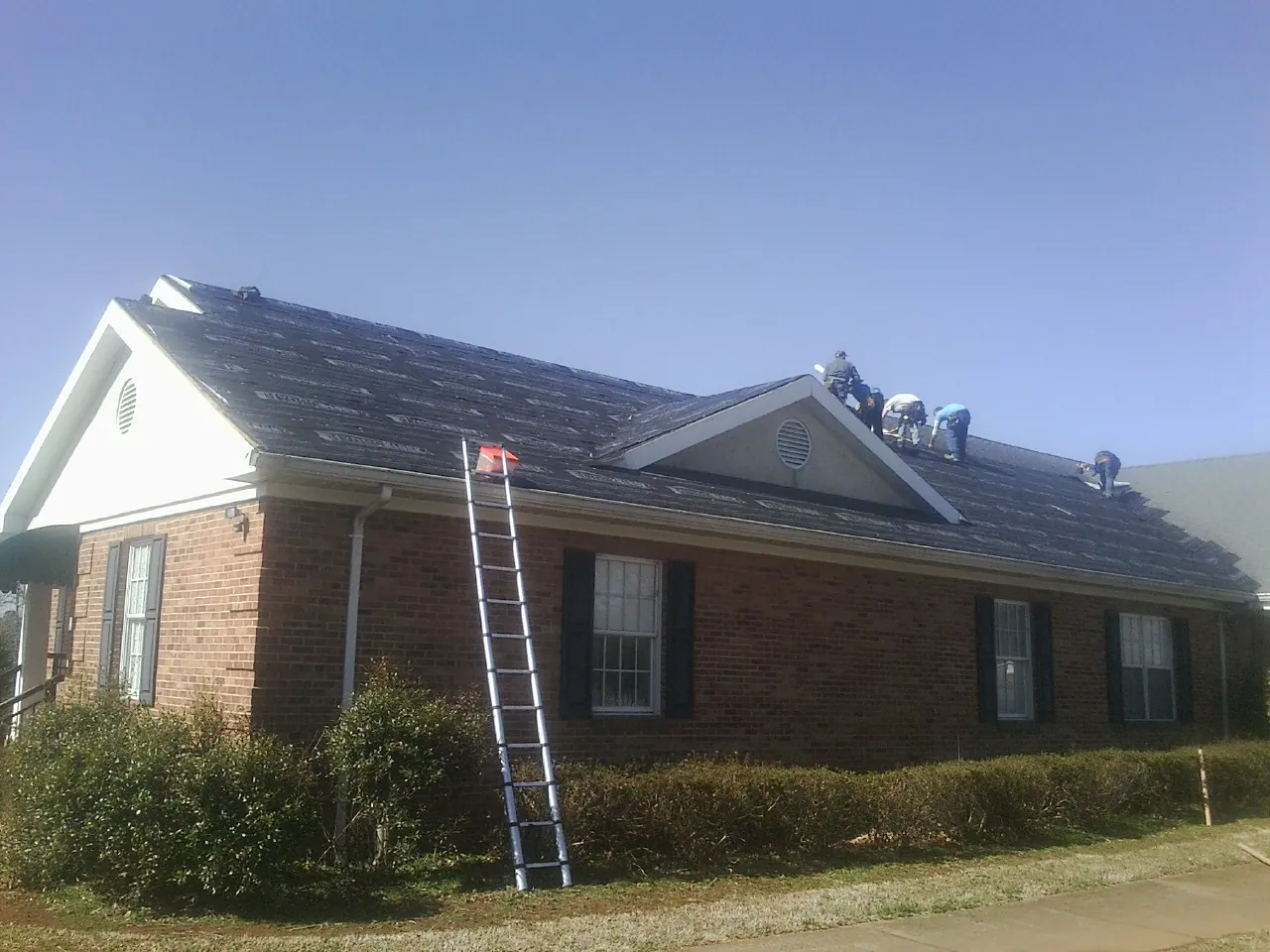 Crew tearing shingles off a brick ranch roof with a ladder set — Emergency Roof Repair work by our crew in Kenton