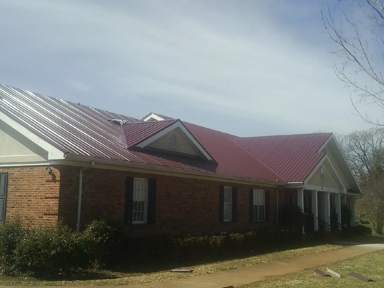 Red metal roof with gabled entries on a long brick building, from a Hail Damage Roof Repair job in Kenton