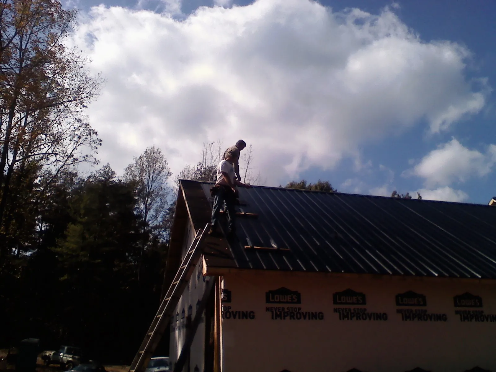Roofer fastening dark metal panels high against a cloudy sky, from a Roof Inspection job in Kenton